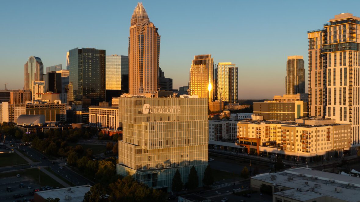 City skyline at sunset with a prominent building labeled "University of North Carolina Charlotte" in the foreground.