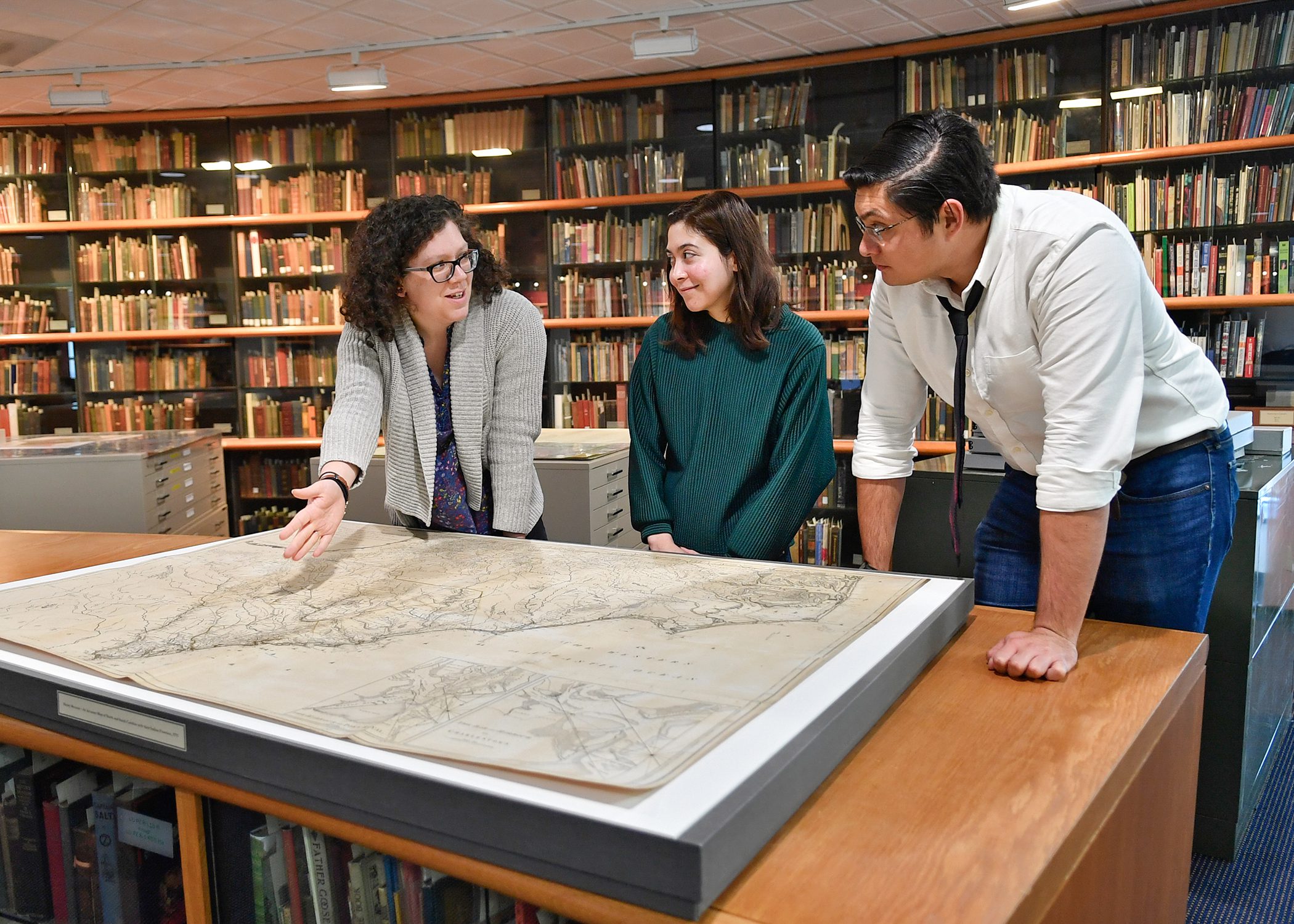 Three people discussing a large map in a library.