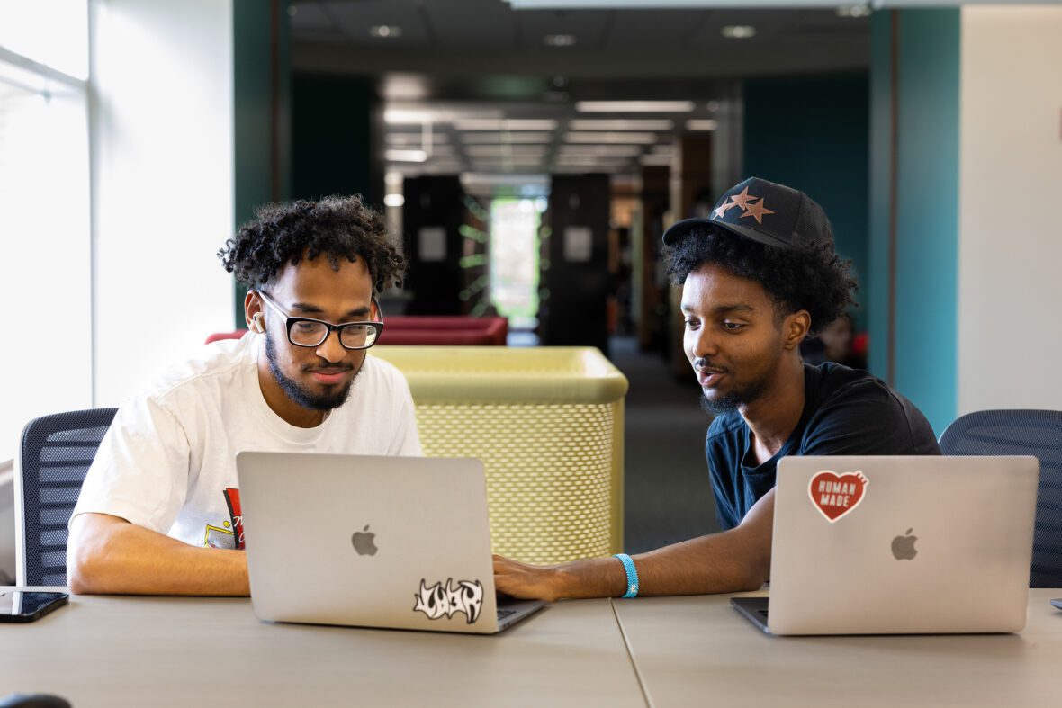 two students studying in the library with laptops