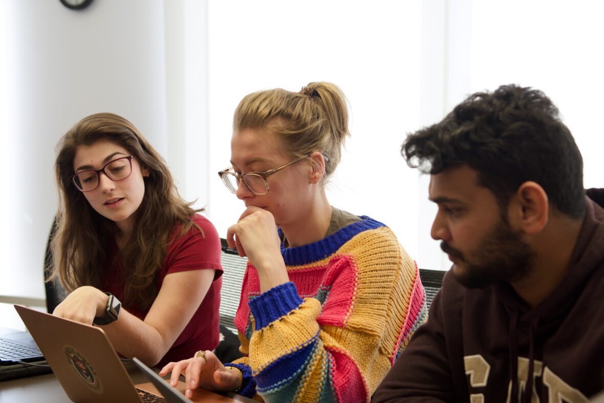 Three students from the Belk College of Business working around a computer