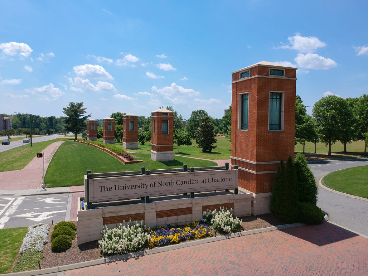 University of North Carolina at Charlotte entrance sign surrounded by flowers and brick pillars beneath a bright blue sky.
