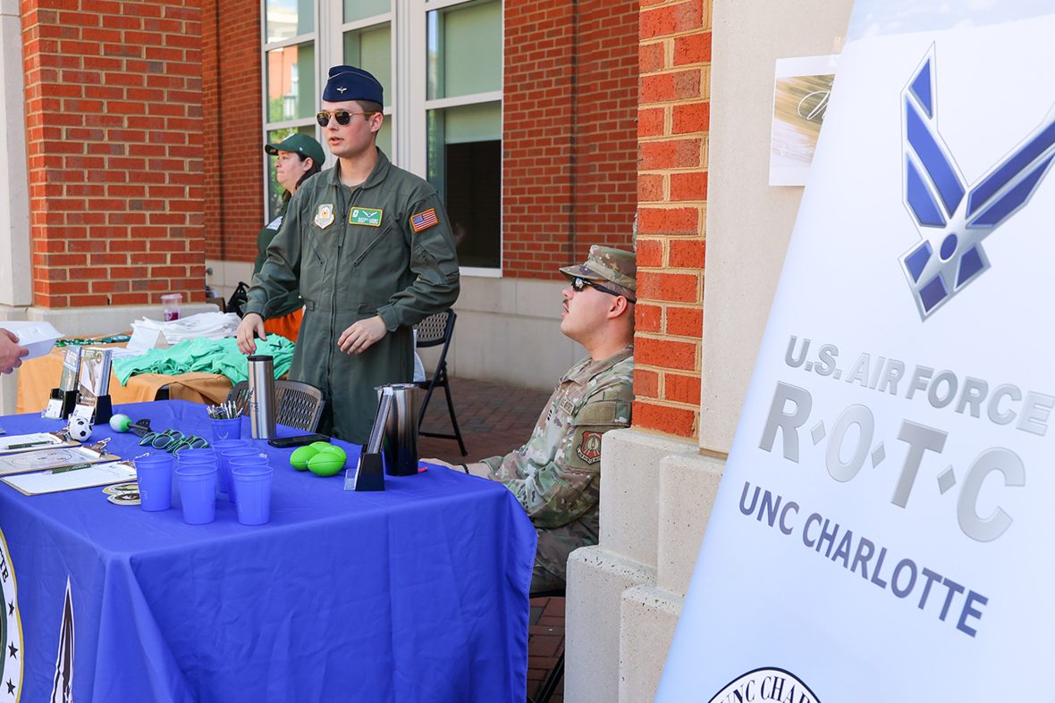 A person in casual attire speaks with U.S. Air Force ROTC representatives at an outdoor information booth on a brick-paved walkway.